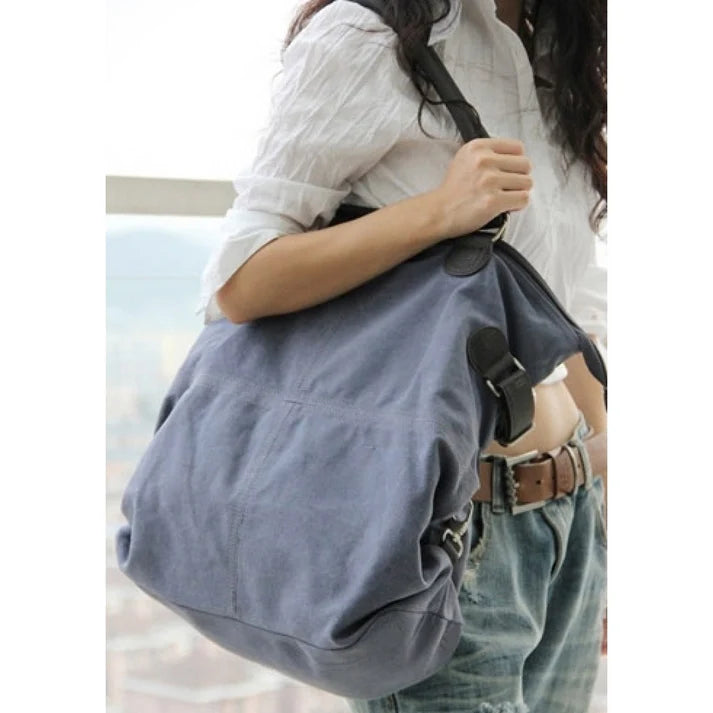 Woman wearing a white collared shirt and blue jeans with a brown leather belt, carrying a large blue canvas bag over her shoulder.