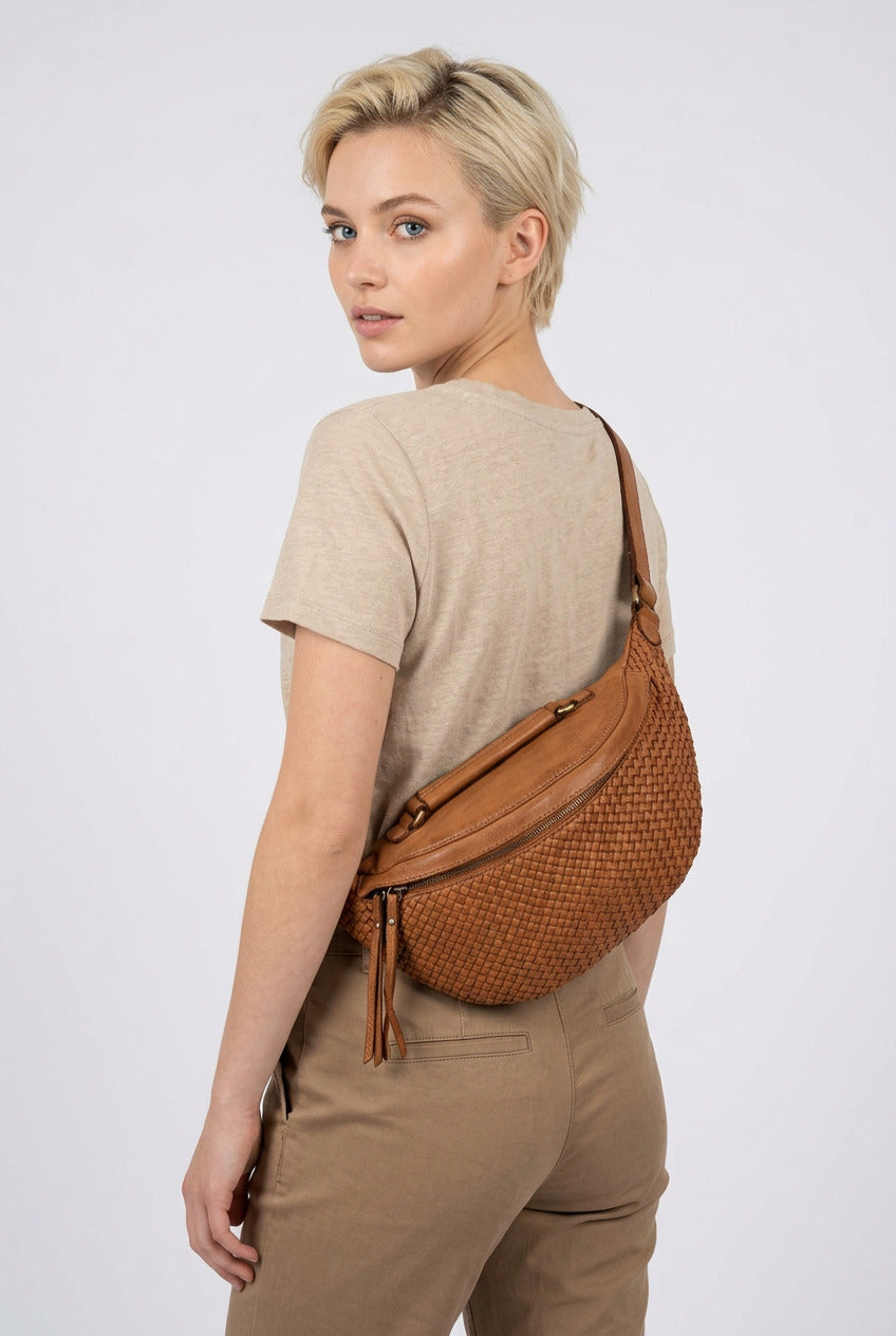Damväska i cognacbrunt flätat italienskt läder, justerbar rem och halvmåneform, bärs crossbody på ryggen
