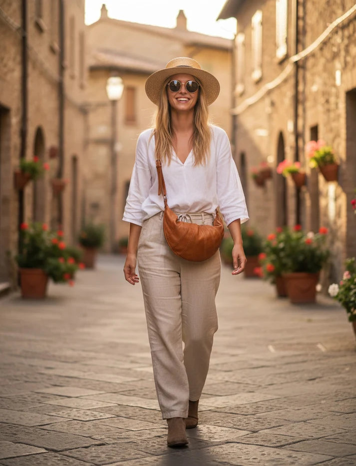 Kvinna bär en halvmåneformad läderväska i konjaksfärg under en promenad på gatan. Brun konjaksfärgad crossbody-väska i italienskt läder kompletterar en ljus, avslappnad outfit.