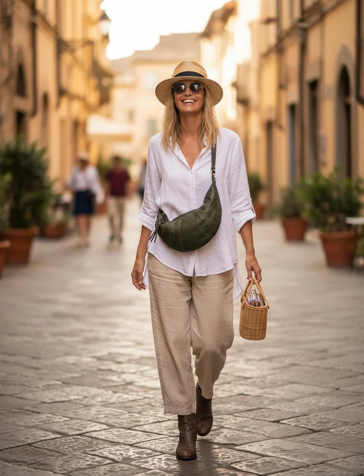 Kvinna promenerar på gatan med en grön halvmåneformad handväska i italienskt läder över axeln. Damens crossbody-väska passar bra med neutrala klädfärger.